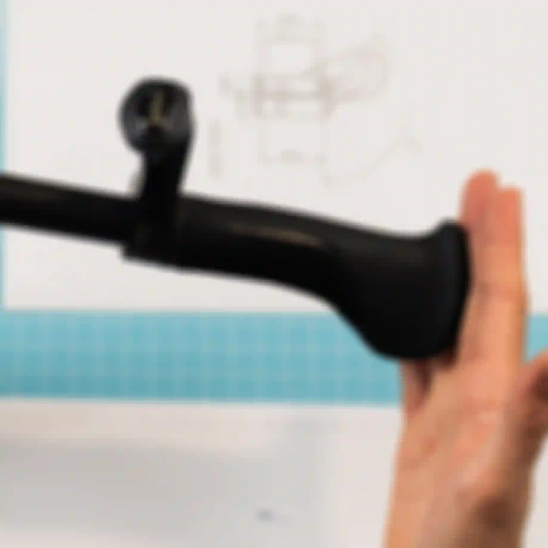 A hand holds a black bicycle handlebar with ergonomic grip over a design blueprint on a light blue grid-patterned table.