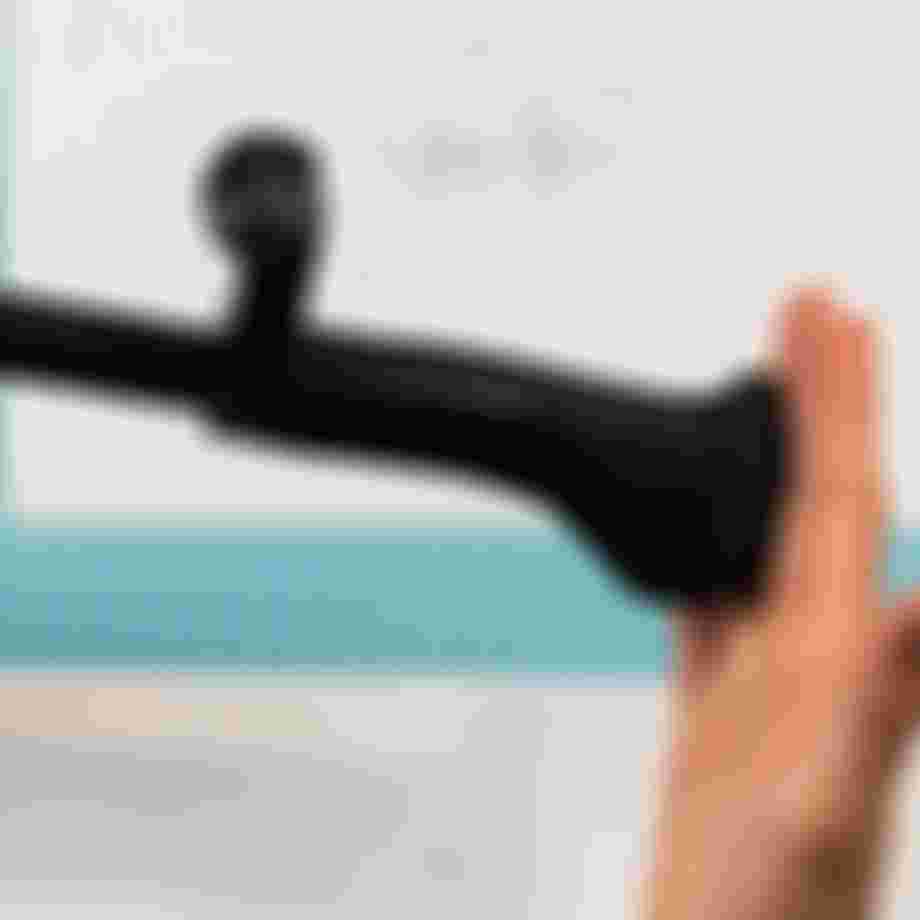 A hand holds a black bicycle handlebar with ergonomic grip over a design blueprint on a light blue grid-patterned table.