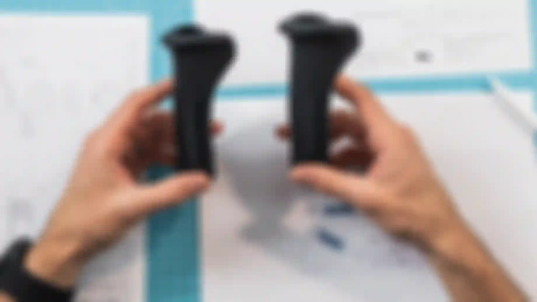 A person holding two black ergonomic handles over blueprints on a blue cutting mat.
