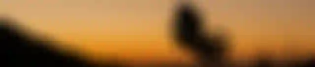 Silhouette of a cyclist mid-jump against an orange sunset sky, with mountain outlines in the background.