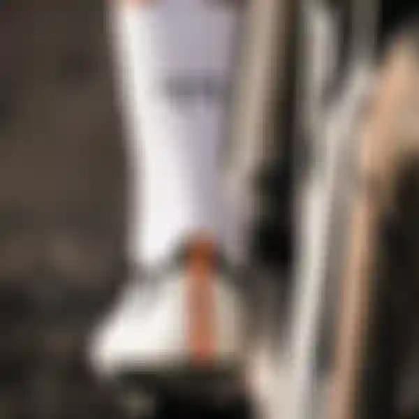 Close-up of a cyclist's foot on a pedal, wearing white socks with "FF" lettering and white cycling shoes with an orange stripe.