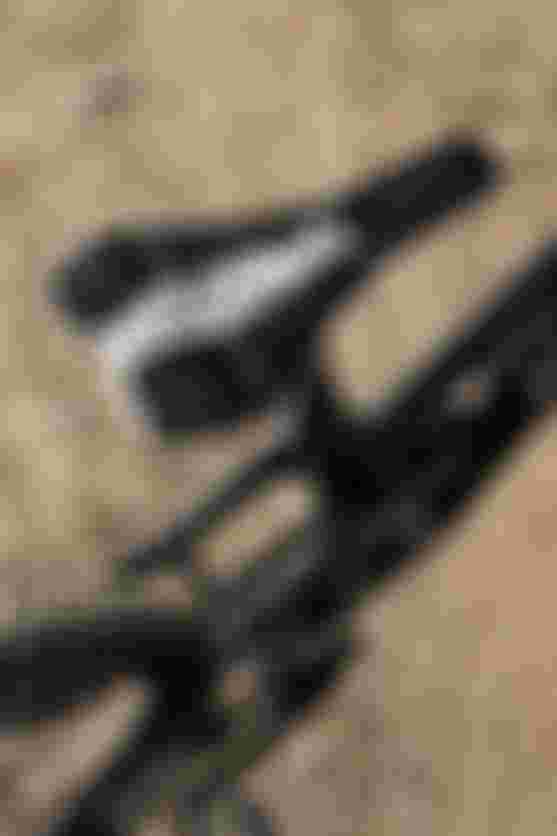 Black and white patterned bicycle saddle on a black bike, viewed from above, with textured dirt ground in the background.