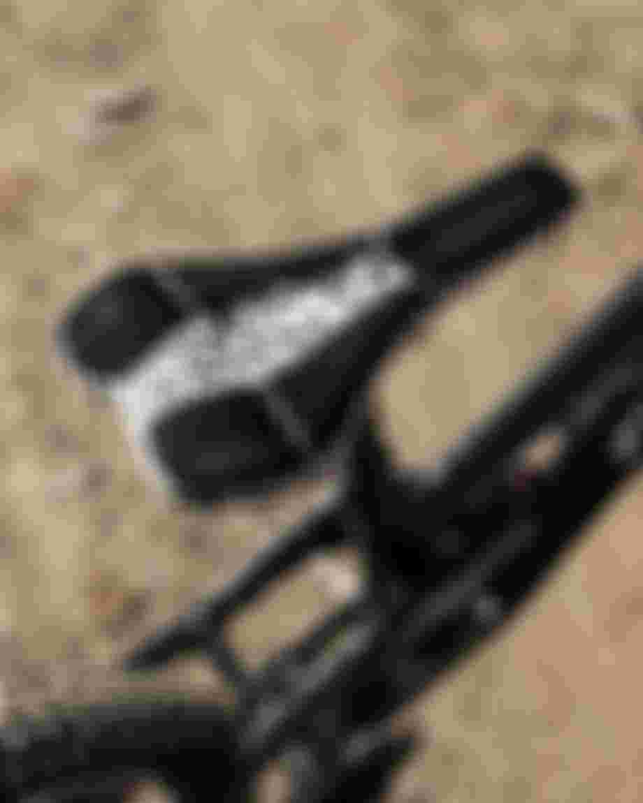 Black and white patterned bicycle saddle on a black bike, viewed from above, with textured dirt ground in the background.