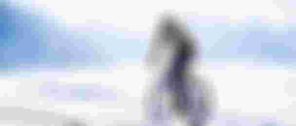 Radsportler fährt mit dem Gravelbike über verschneite Landschaft vor Bergkulisse.“