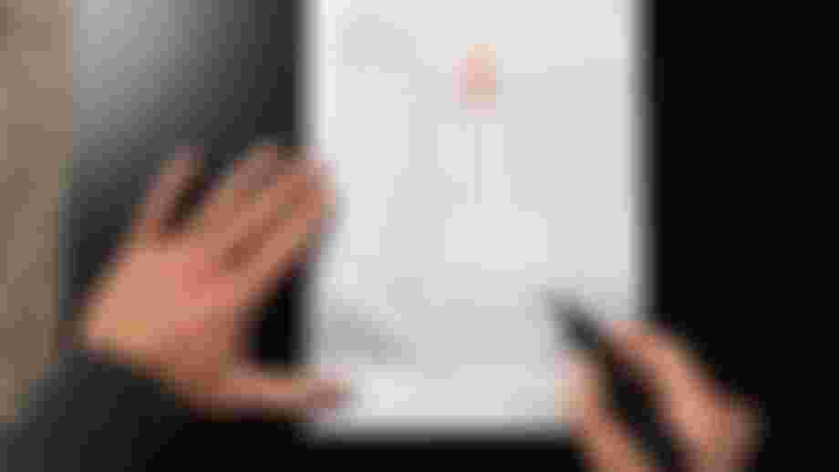 Person measuring hand size with a printed guide on a dark surface, using a marker to indicate dimensions on a diagram of a hand.