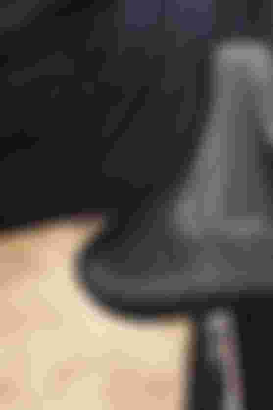 Close-up of a black bicycle saddle with ergonomic design and branding details, mounted on a bike. A person wearing dark clothing is partially visible.