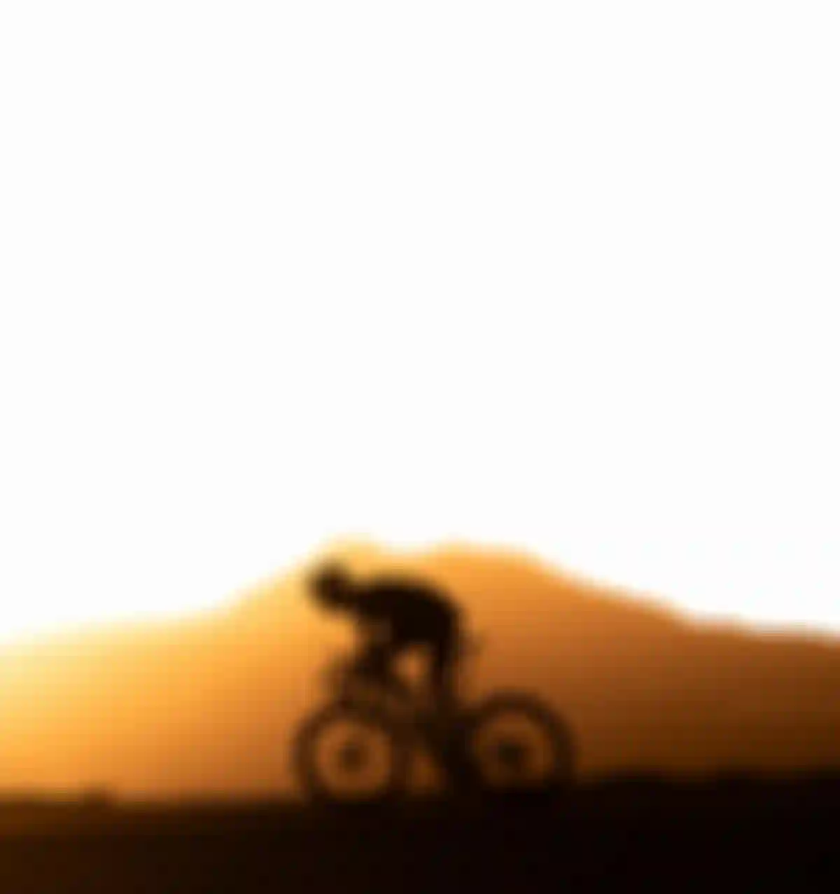 Silhouetted cyclist rides against a vibrant orange sunset, with a mountain in the background.