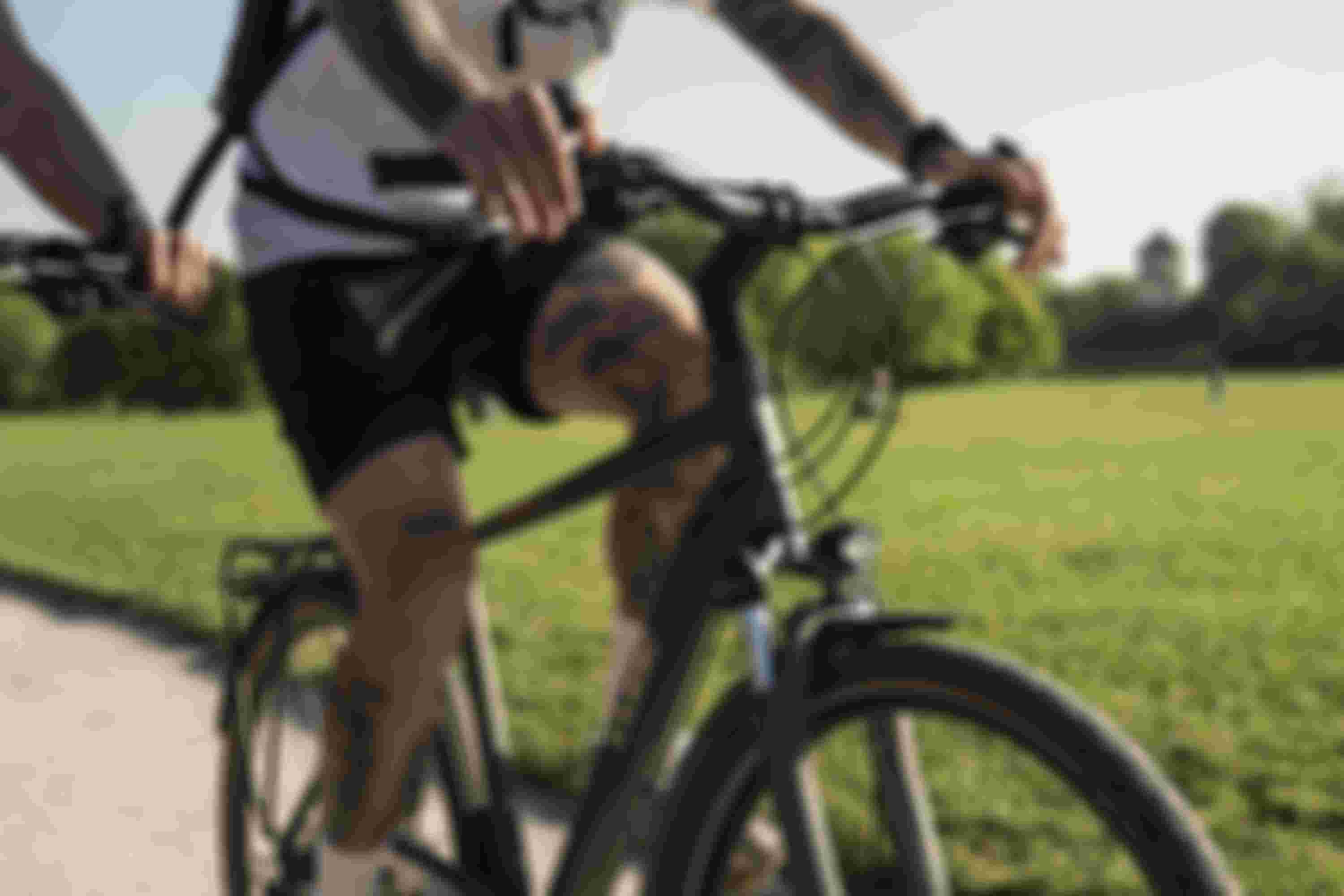 Close-up of a tattooed person riding a bicycle on a sunny day, with a lush green park in the background.