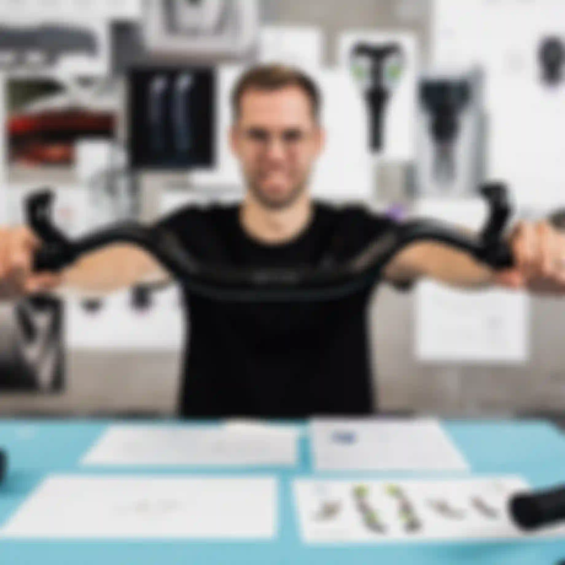 Product developer holding a SQlab bicycle handlebar with ergonomic grips at a design workspace with technical drawings and prototypes in the background.