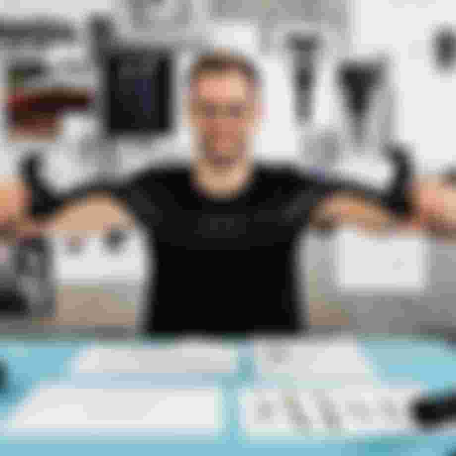 Product developer holding a SQlab bicycle handlebar with ergonomic grips at a design workspace with technical drawings and prototypes in the background.