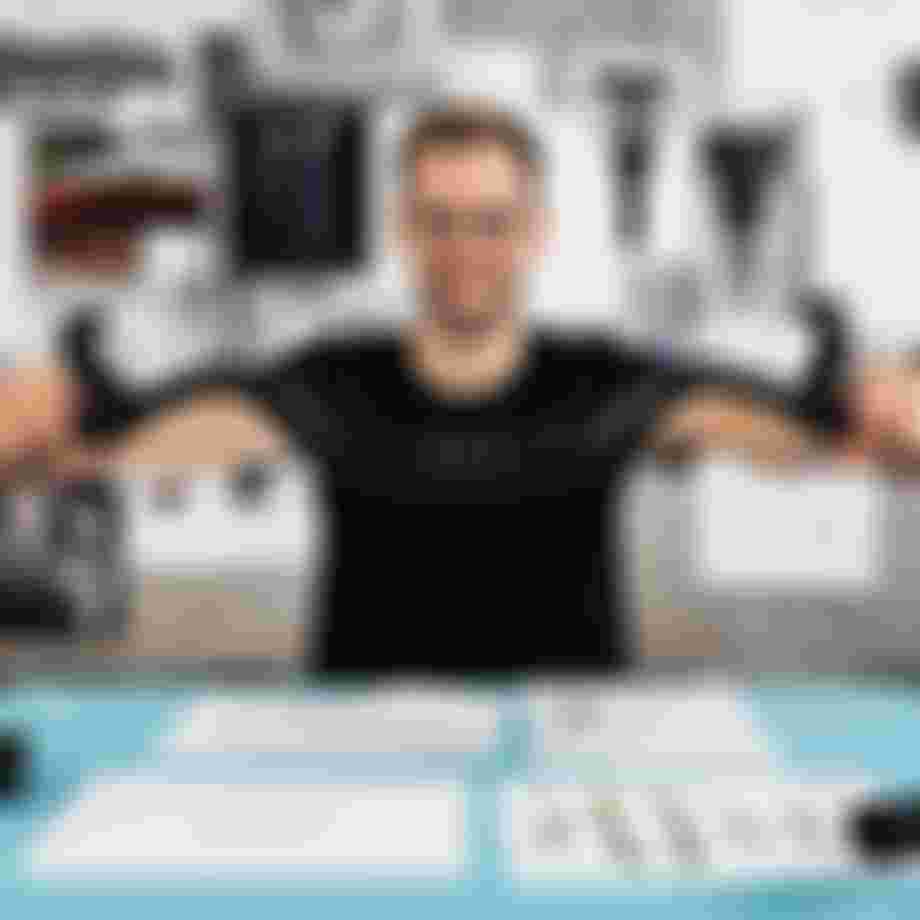 Product developer holding a SQlab bicycle handlebar with ergonomic grips at a design workspace with technical drawings and prototypes in the background.