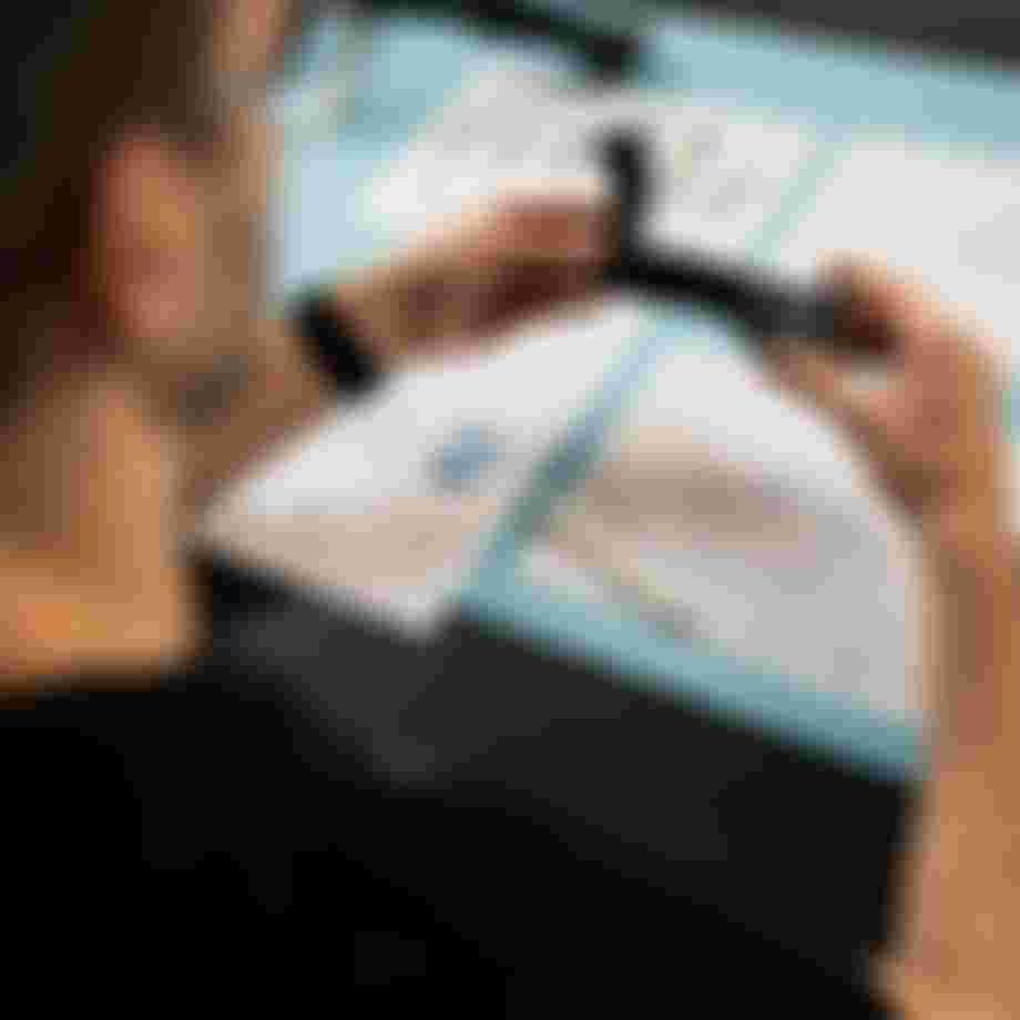 Top view of hands holding a SQlab ergonomic bicycle grip prototype over technical design drawings on a workbench.