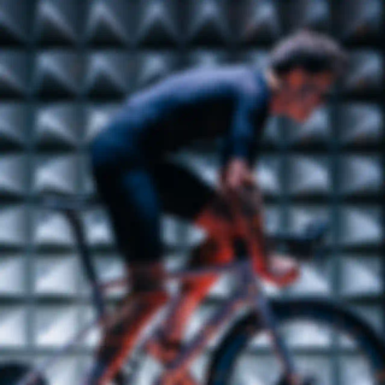 Cyclist on a stationary bike in anechoic chamber, wearing a fitted black outfit, with grid pattern lighting effects.