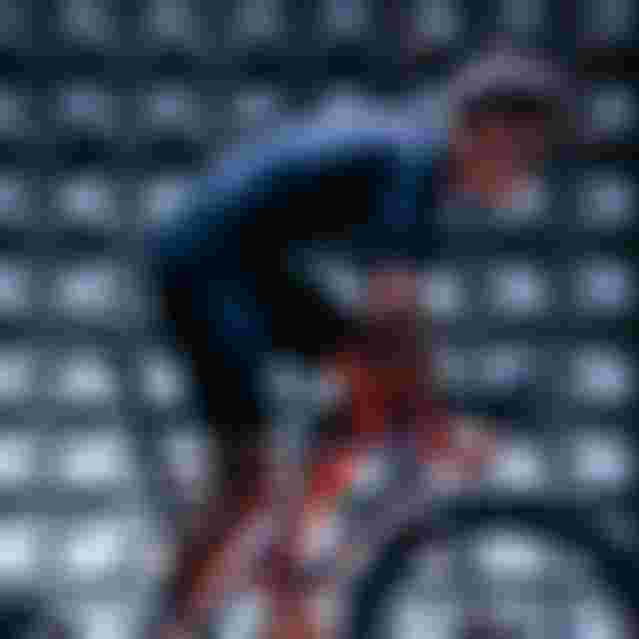 Cyclist on a stationary bike in anechoic chamber, wearing a fitted black outfit, with grid pattern lighting effects.