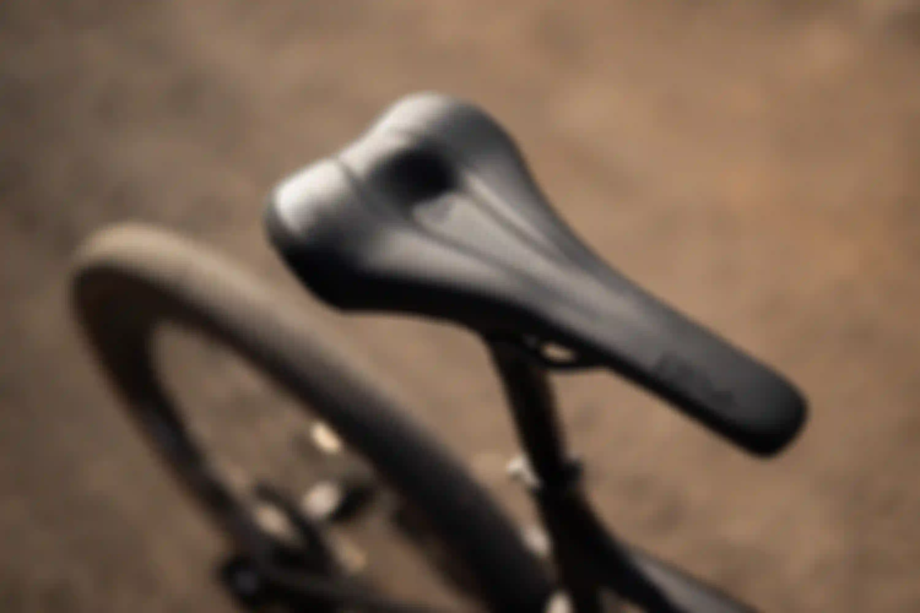 Close-up of a black bicycle saddle with perforated design and branding, mounted on a bike, with blurred background.