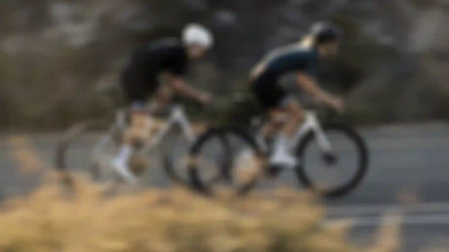 Zwei Rennradfahrer auf einer Straße, seitlich fotografiert mit Bewegungsunschärfe.