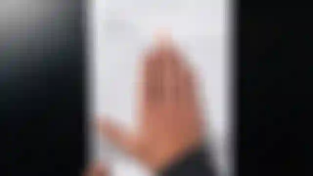 Hand measuring grip width on a measurement guide, with an orange arrow pointing at the fingertips. Text in German is visible on the paper.