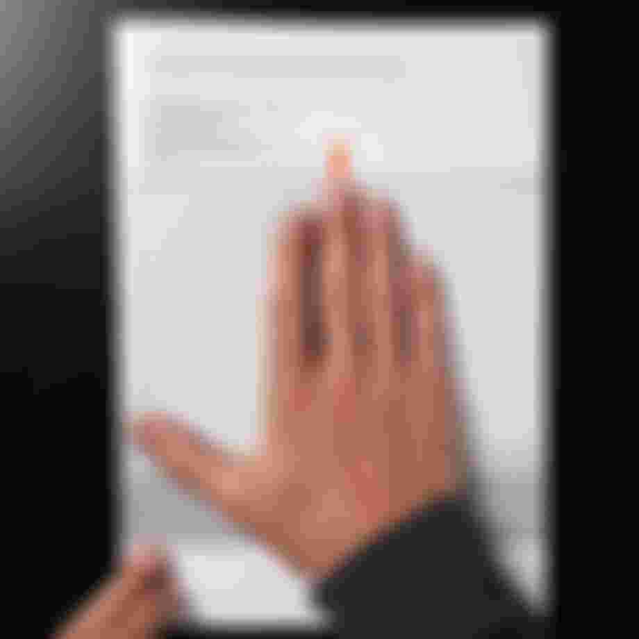 Hand measuring grip width on a measurement guide, with an orange arrow pointing at the fingertips. Text in German is visible on the paper.