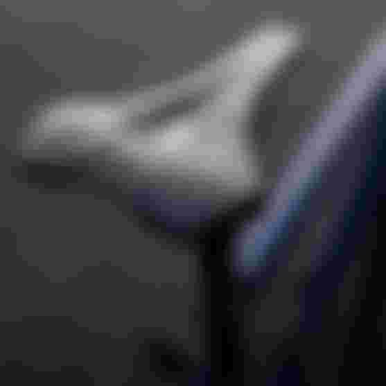 Close-up of a sleek black bicycle seat with a subtle logo, set against a blurred dark background.