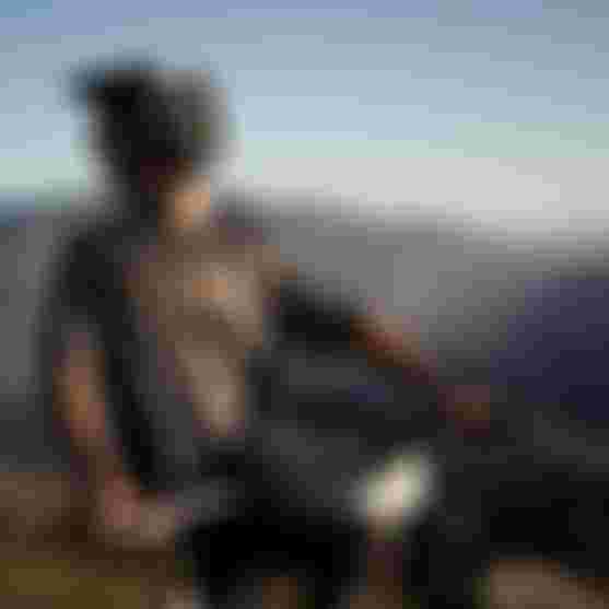 Mountain biker in protective gear resting on a bike with a scenic mountain landscape in the background at sunset.