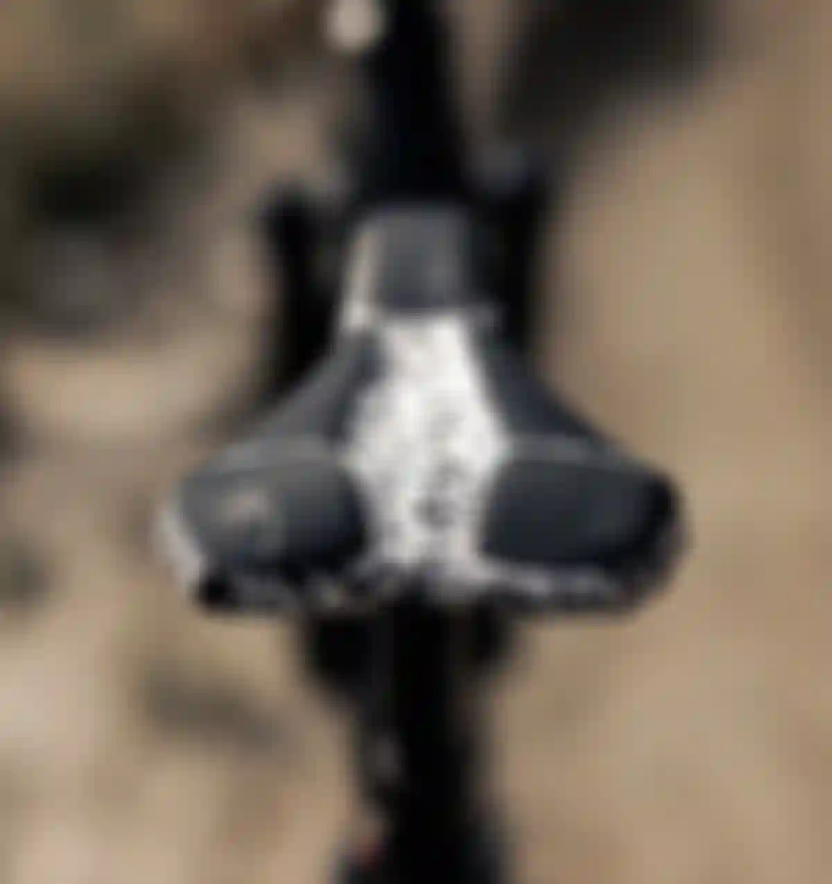 Close-up of a bicycle seat with a black and white speckled pattern, featuring a small logo on the front, set against a blurred outdoor background.