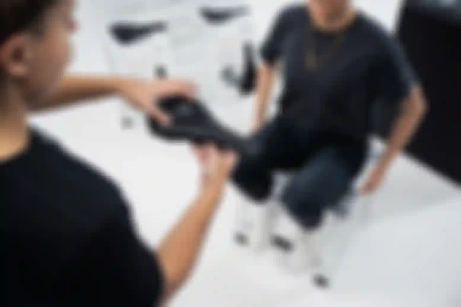 Person holds a bicycle saddle while another sits on a fitting tool, discussing comfort options in a bright store.
