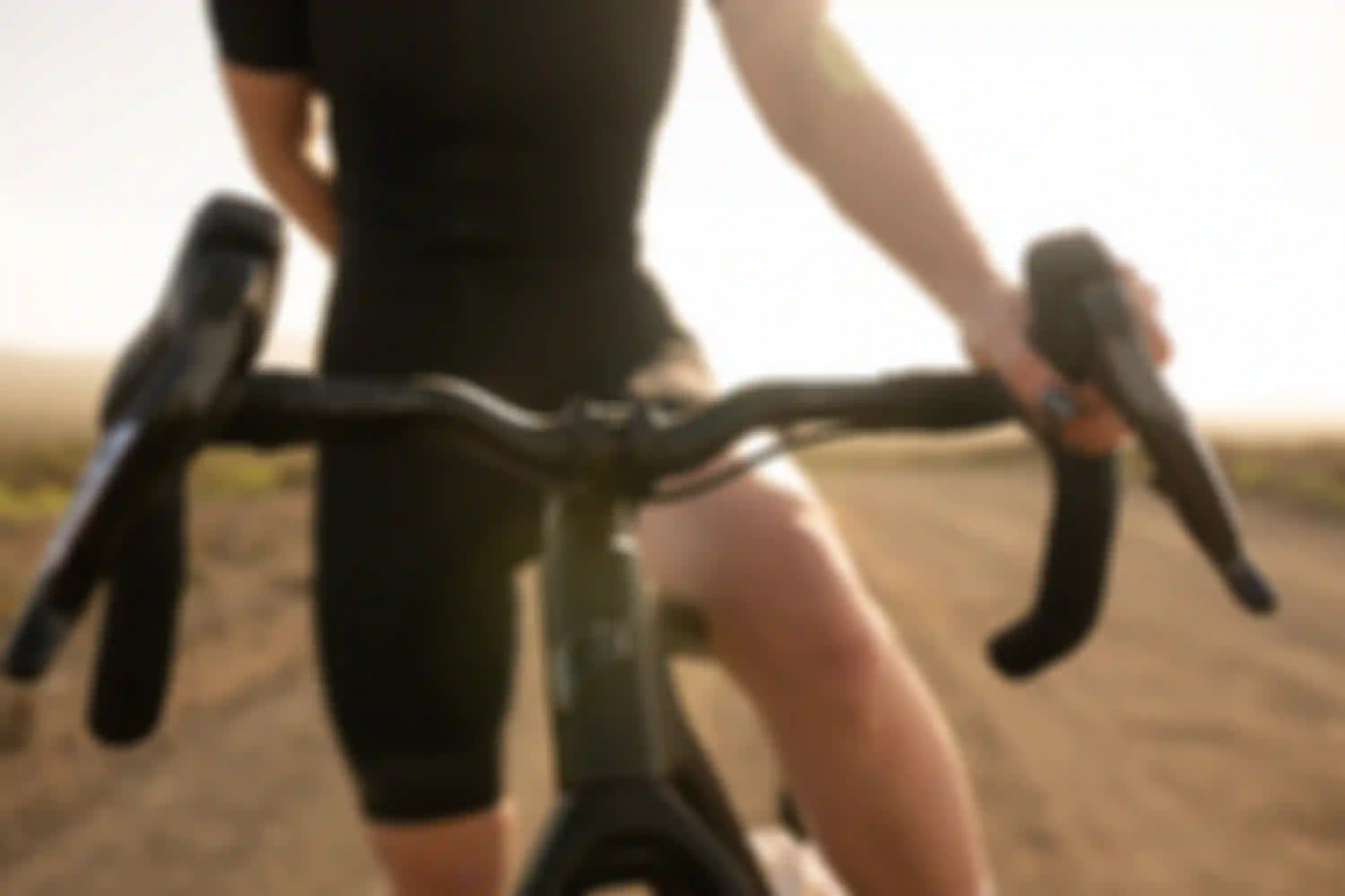 A person wearing a black outfit holding the handlebars of a bicycle on a sunlit dirt road.