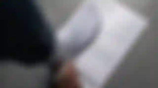 Person wearing a white sock is tracing their foot on a piece of paper with foot measurements and instructions on a gray surface.