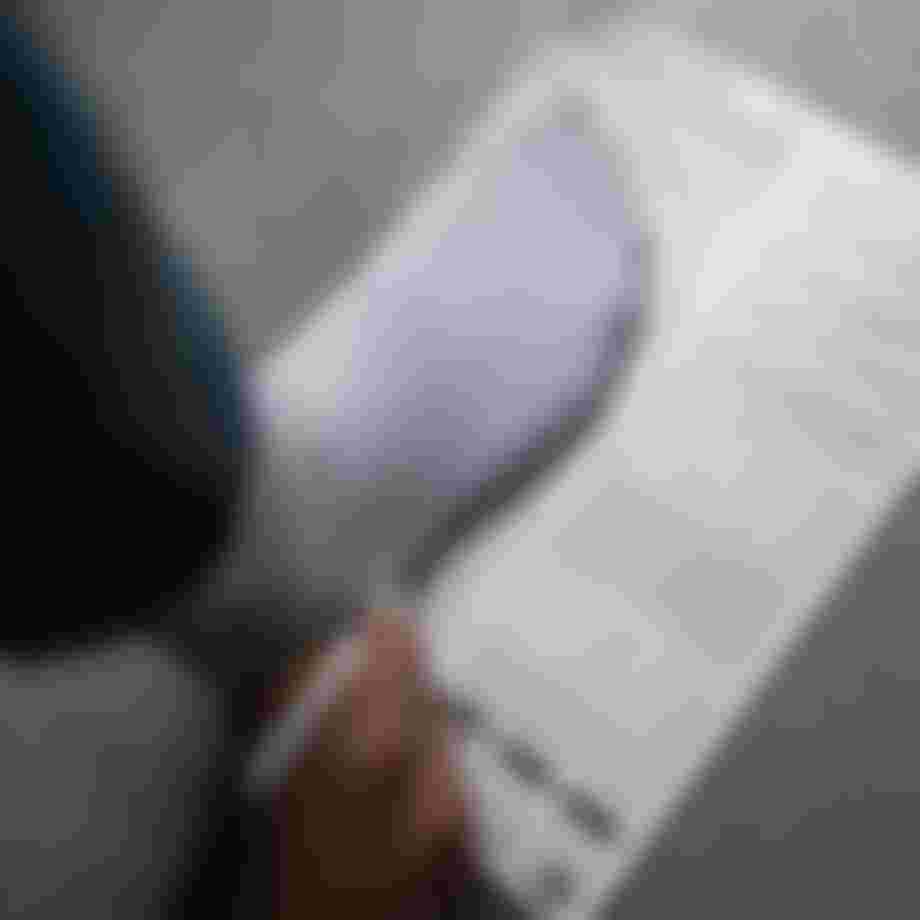 Person wearing a white sock is tracing their foot on a piece of paper with foot measurements and instructions on a gray surface.