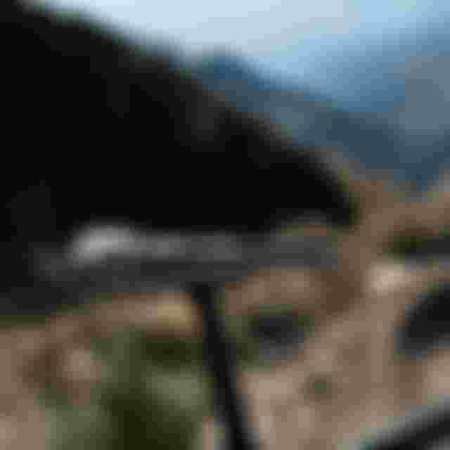 Close-up of a bicycle saddle with a black and white pattern, set against a blurred mountainous landscape under a bright sky.