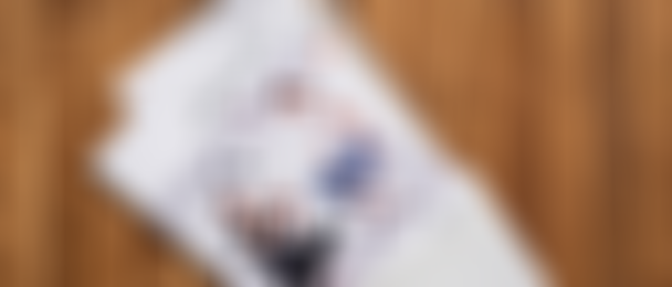 Open envelope lying on a wooden floor with a partially pulled-out “Family & Friends Vermessungs-Set” booklet showing two people sitting on measuring boxes.