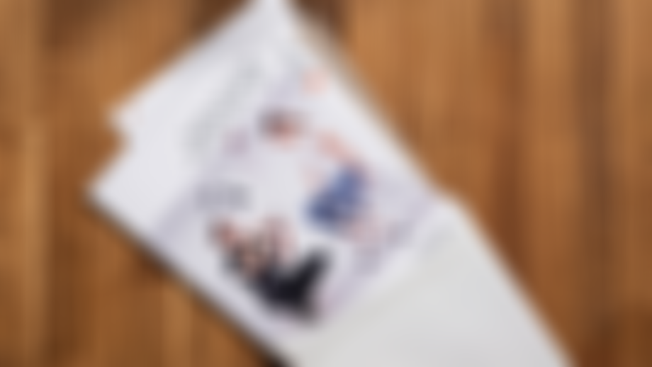 Open envelope lying on a wooden floor with a partially pulled-out “Family & Friends Vermessungs-Set” booklet showing two people sitting on measuring boxes.