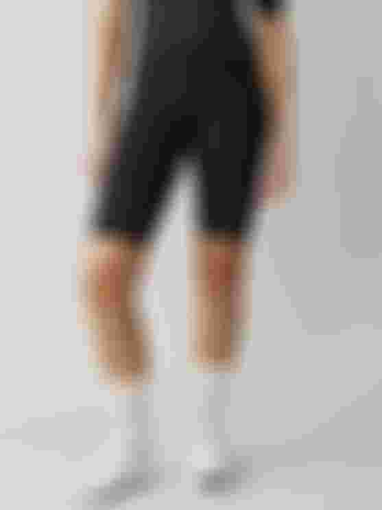 Cyclist wearing black SQlab ONE12 R shorts, standing in a studio against a neutral background, showcasing the leg panels and fit.