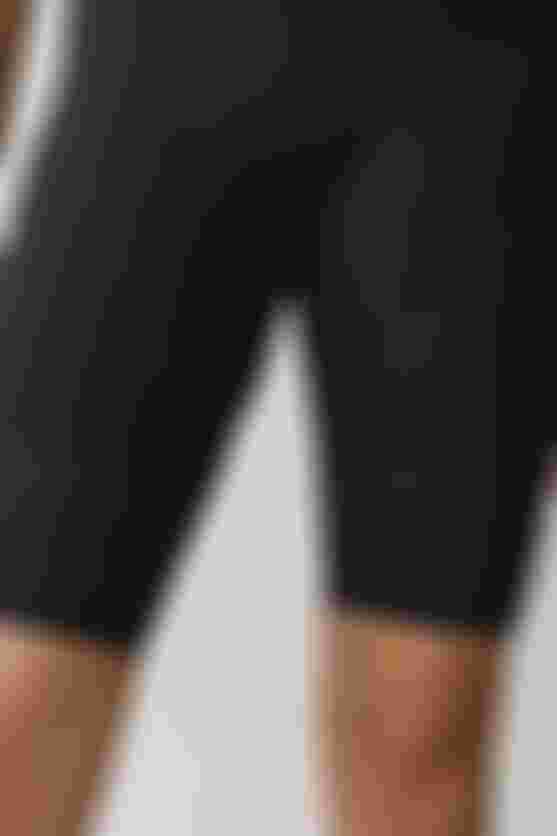 Cyclist wearing black SQlab ONE12 R shorts, standing in a studio against a neutral background, showcasing the leg panels and fit.