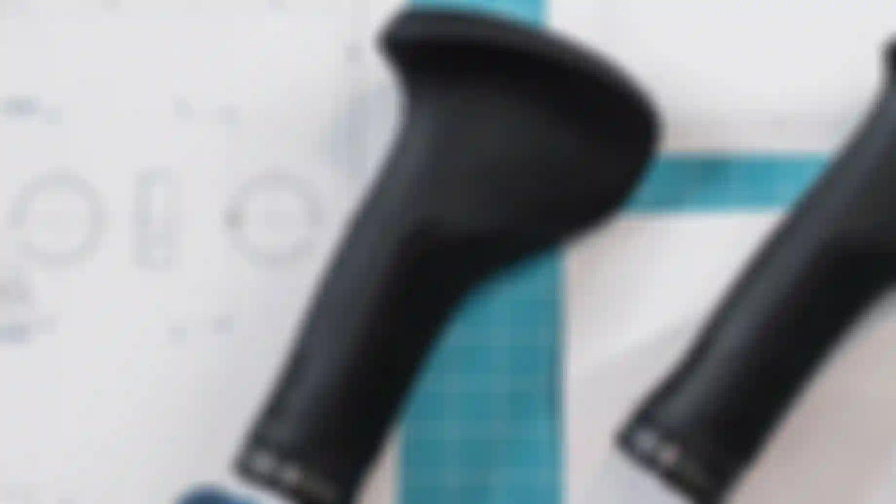 Black ergonomic bicycle grips on a blueprint with a grid cutting mat, showing design and measurements.