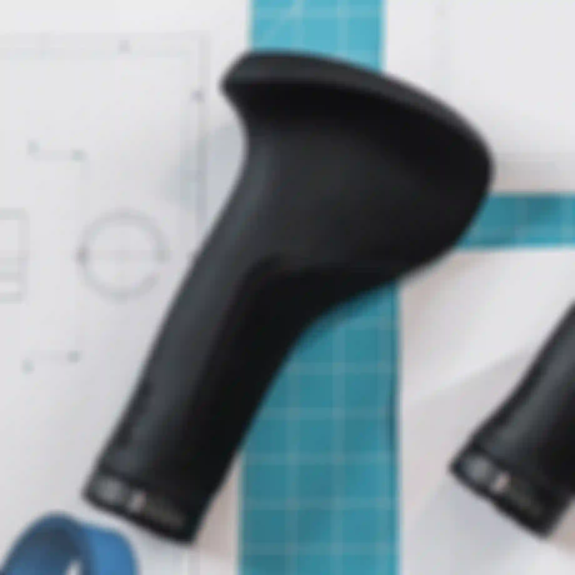 Black ergonomic bicycle grips on a blueprint with a grid cutting mat, showing design and measurements.