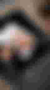 A person in a grey sweater uses a pen to mark a typed document on a black table, with a beige textured carpet underneath.