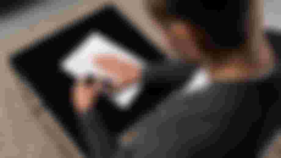 A person in a grey sweater uses a pen to mark a typed document on a black table, with a beige textured carpet underneath.