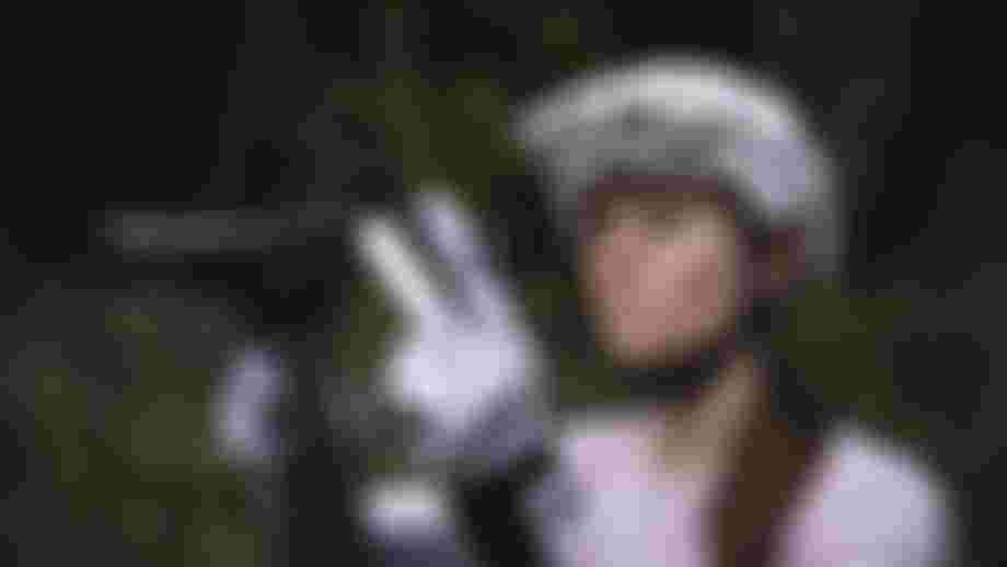 Mountain biker wearing a white helmet and gloves adjusts a bike saddle outdoors, with a blurred forest background.